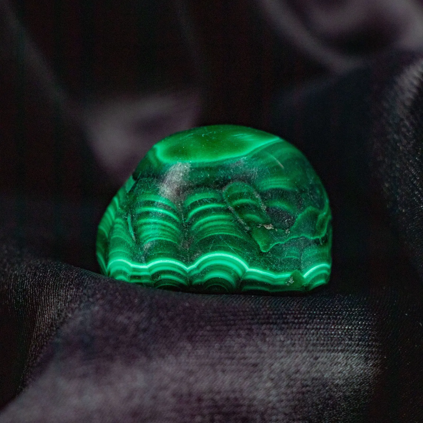 A polished malachite dome resting on black silk, banded in concentric rings of light and dark green
